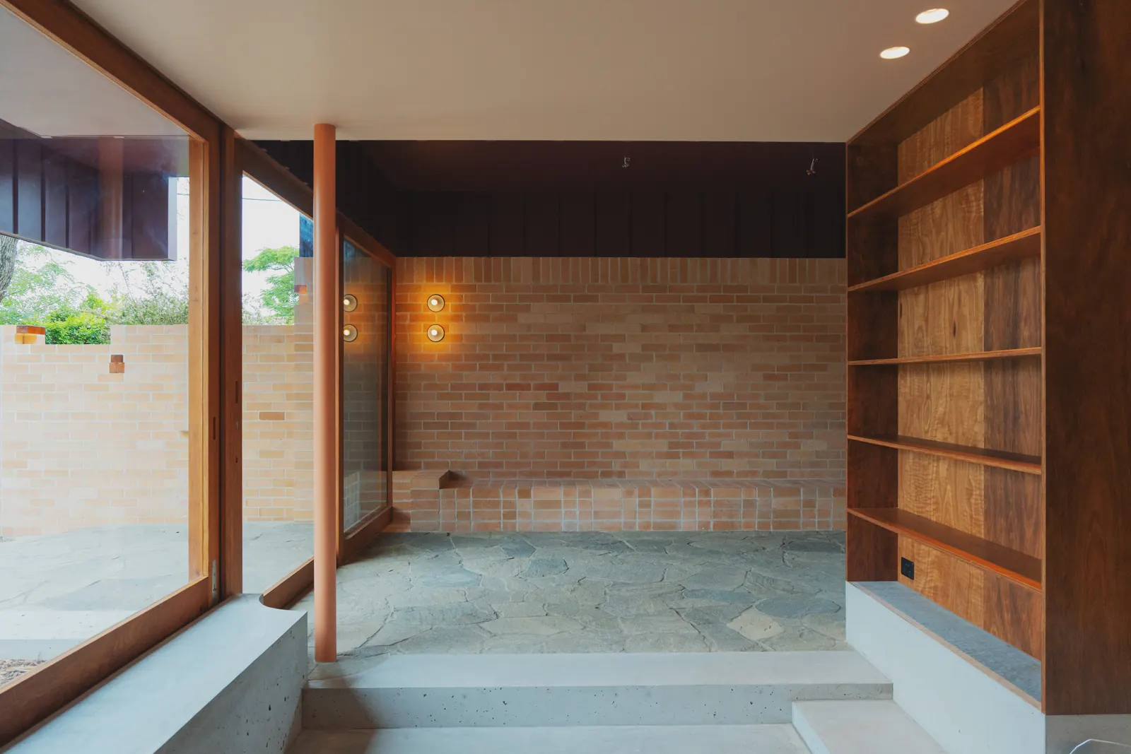 Brick wall with two wall lights beside timber shelving and a stone floor
