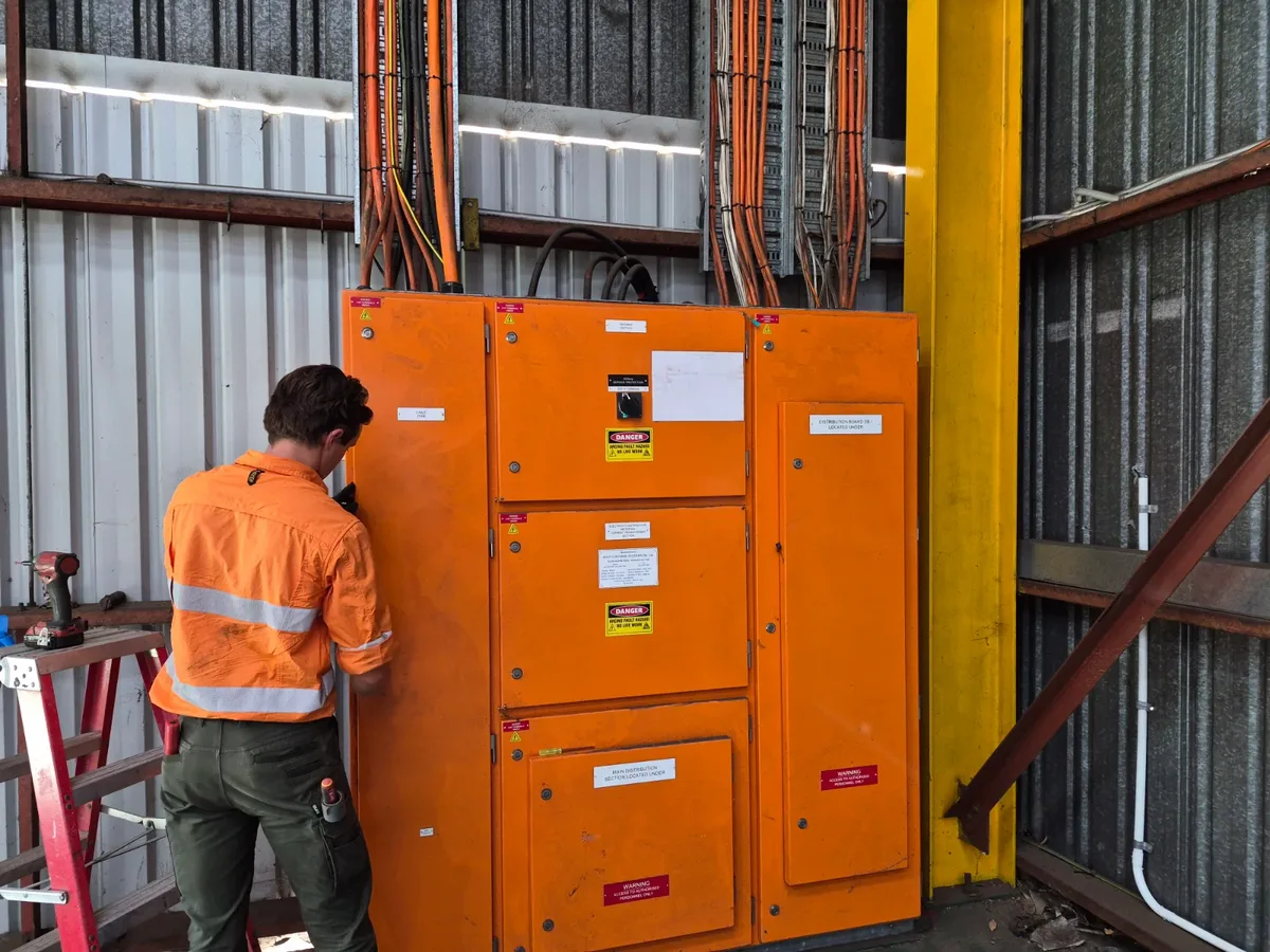 Technician in an orange hi-vis shirt opening an orange electrical switchboard in a metal shed