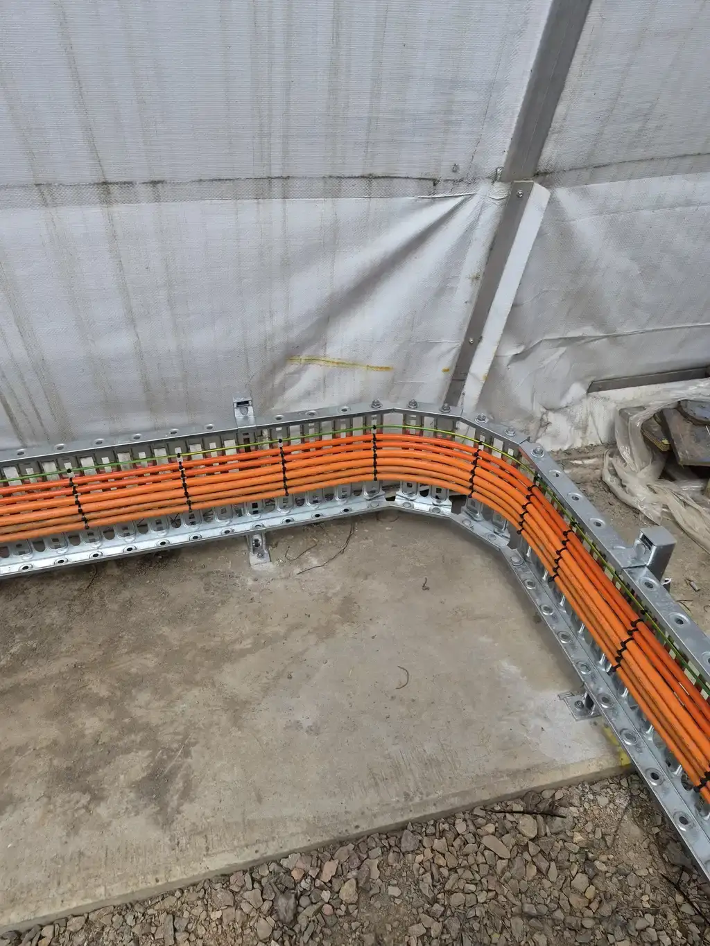 Orange cables running in a galvanised cable tray at the corner of the new building pad