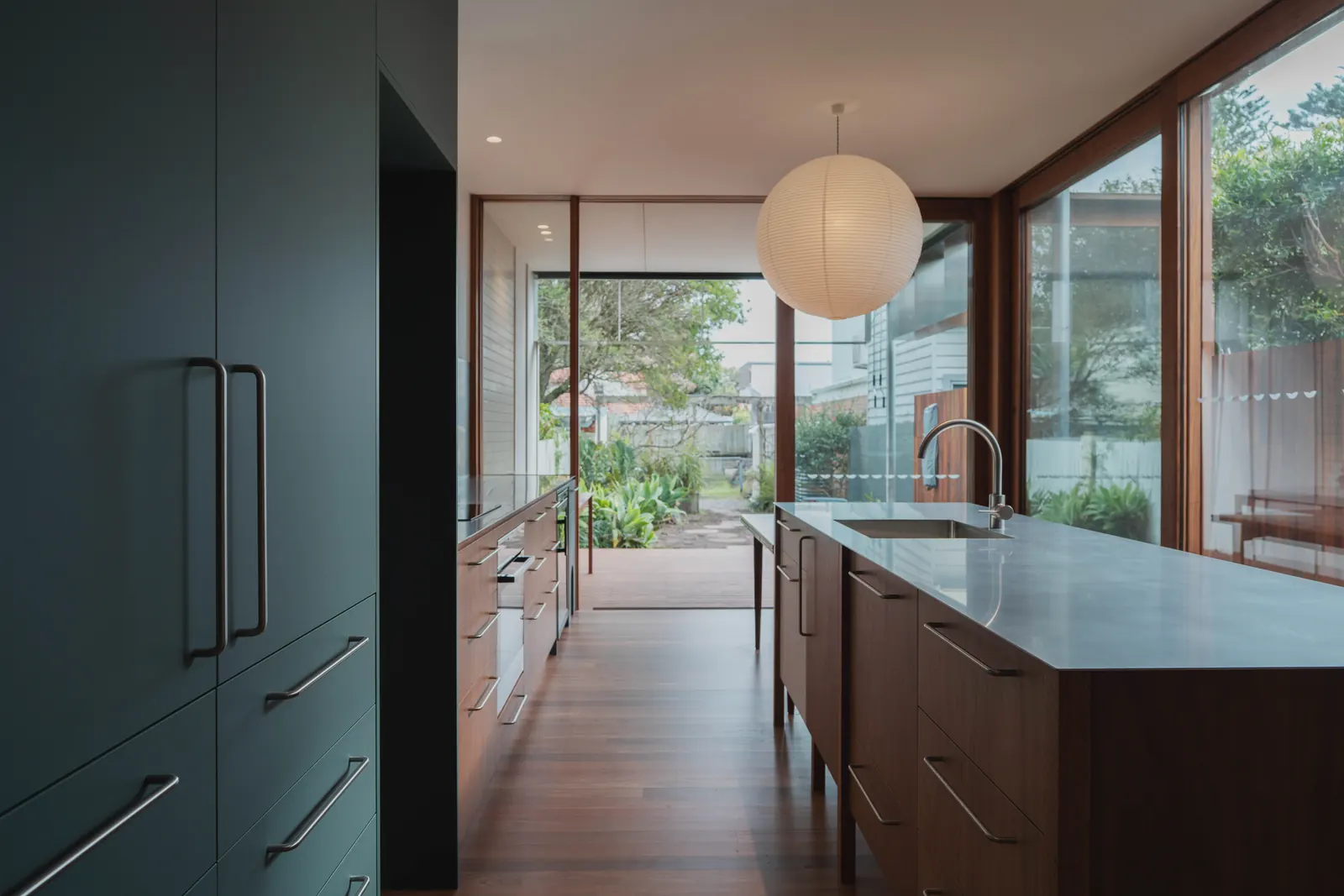 Kitchen island and dark cabinetry under a paper pendant light, with glazing to the garden
