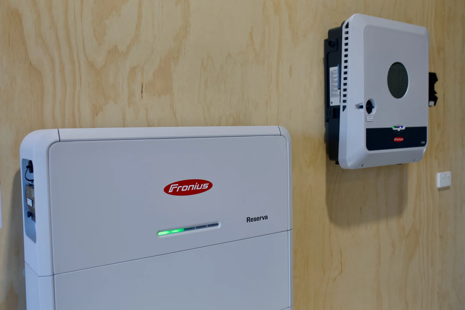 Fronius battery stack and hybrid inverter on the plywood-lined shed wall
