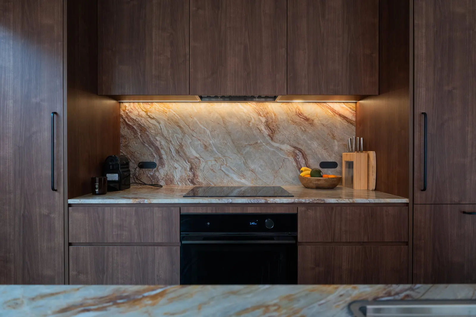 Strip lighting under the overhead cabinets, above the stone splashback