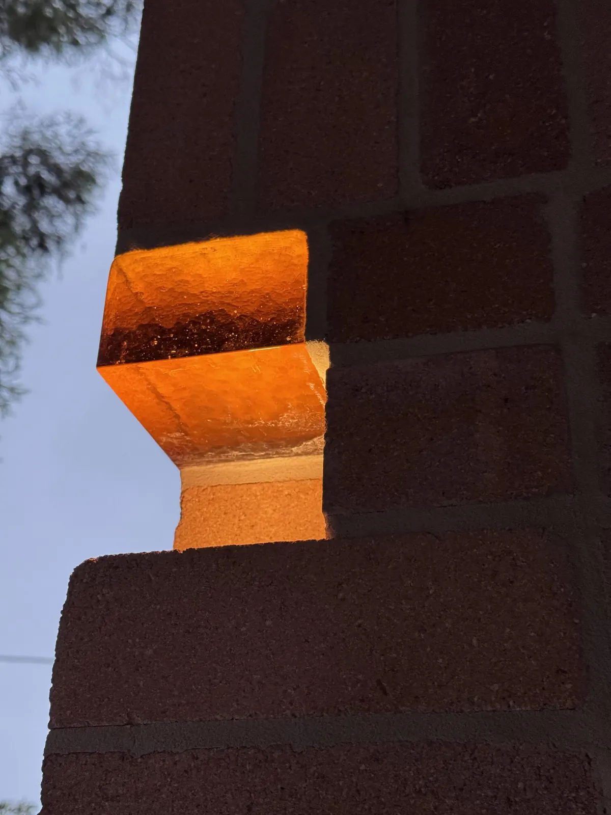 Feature light in the brick wall at dusk, an amber glass block lit from below