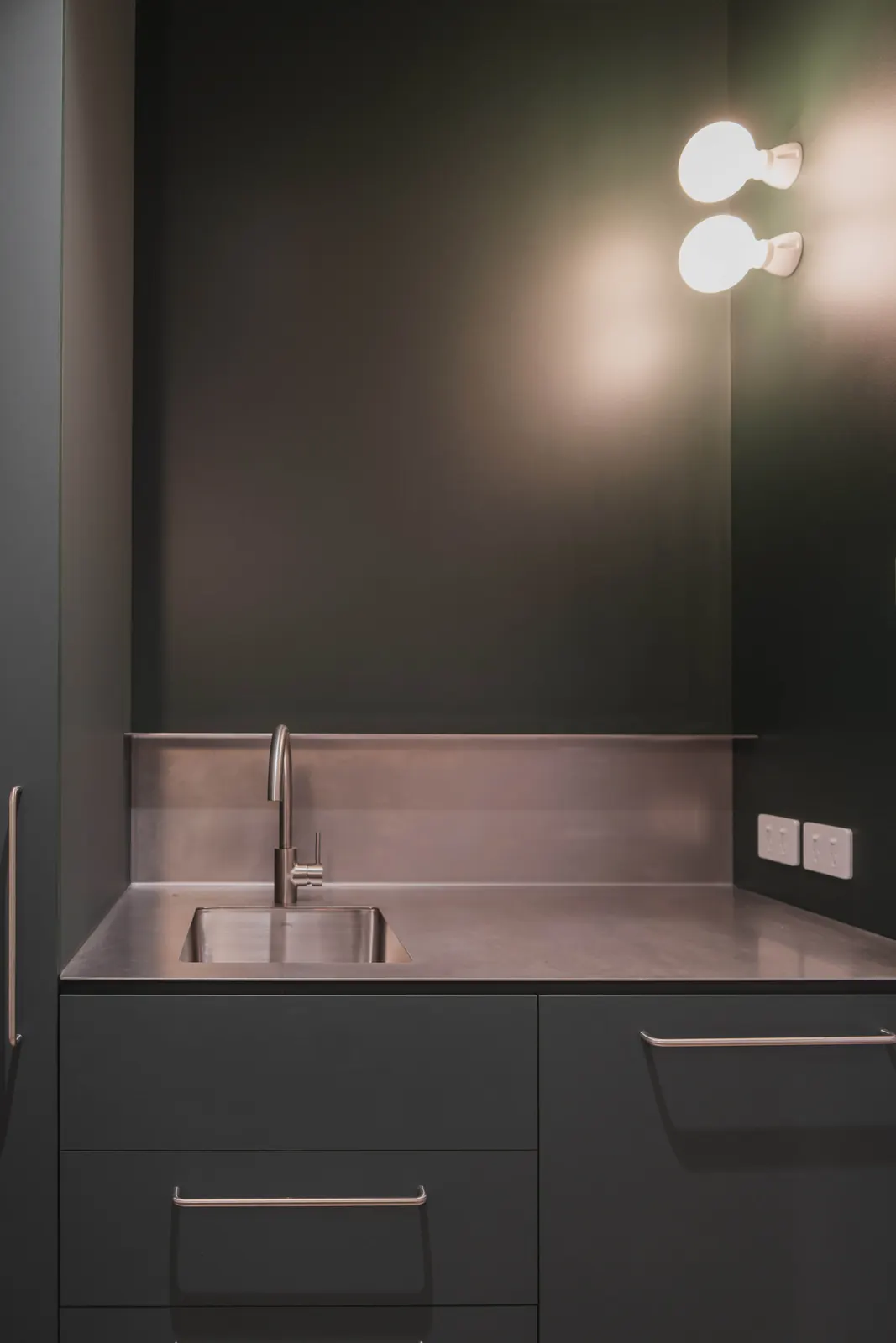 Globe wall lights and power outlets above a stainless steel bench